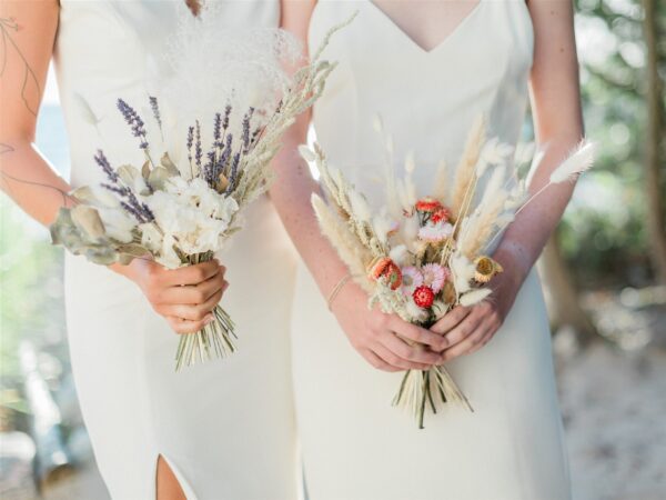 Two bridesmaids holding bouquets in white dresses.