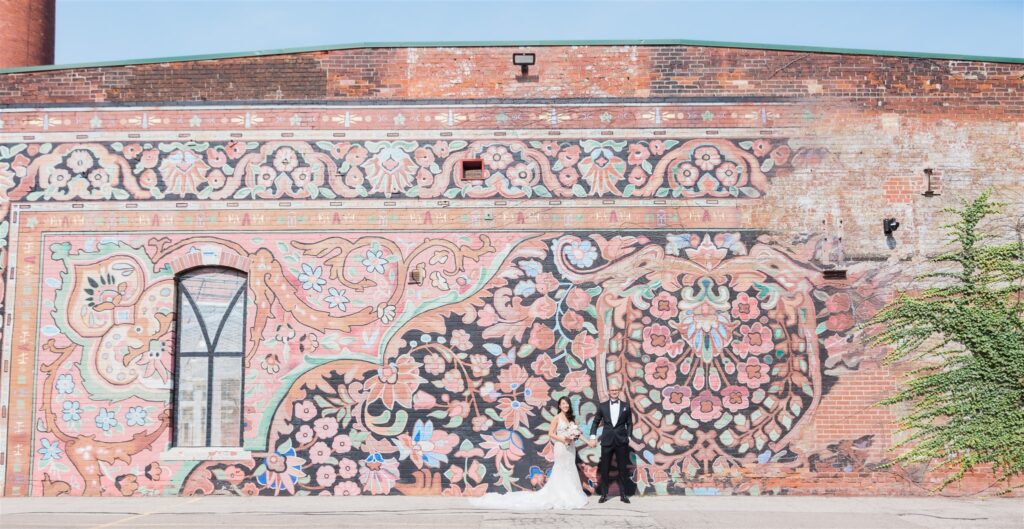 bride and groom pose in front of large wall mural for wedding photos