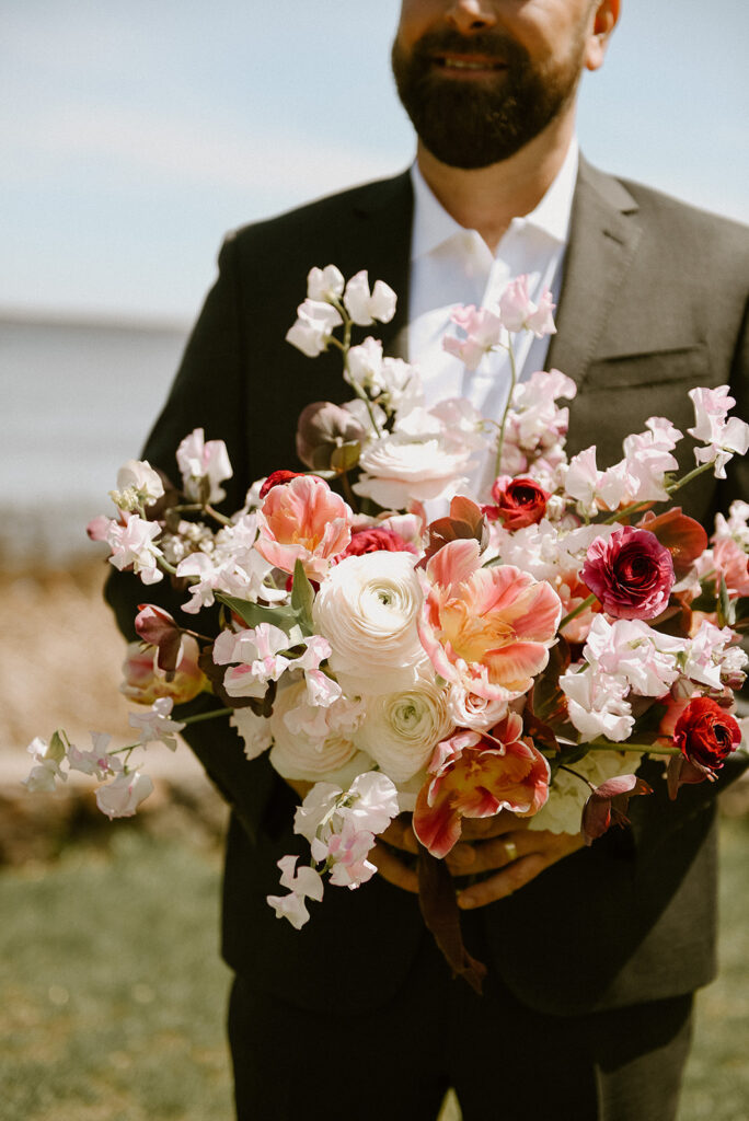 Groom holding a bouquet of different white, pink and red Hellebores