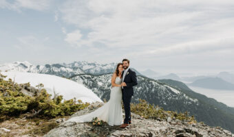 bride and groom pose on mountaintop with snow capped background at the best honeymoon destination - Goat Ridge,Tantalus Mountain Range