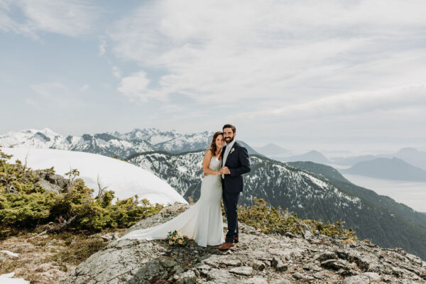 bride and groom pose on mountaintop with snow capped background at the best honeymoon destination - Goat Ridge,Tantalus Mountain Range