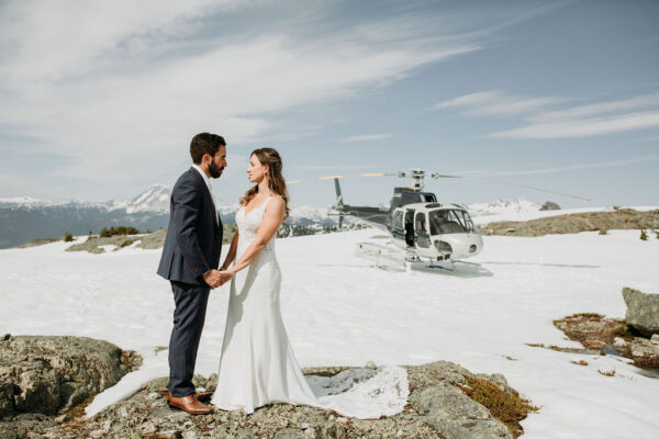 bride and groom pose for picture in front of helicopter wedding transportation