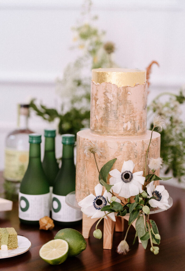 An elegant wedding cake featuring tastefully arranged green floral decorations, complemented by a bottle of champagne for toasting.