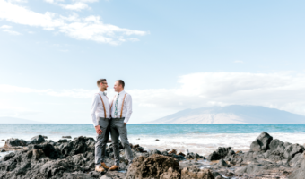 two grooms pose on volcano rocks in Maui at destination wedding