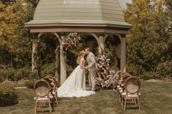 bride and groom kiss in front of gazebo decorated with beautiful flowers