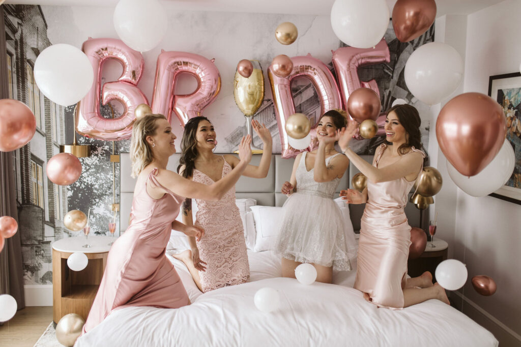 bride and bridesmaid kneeling on bed with big pink BRIDE balloons backdrop