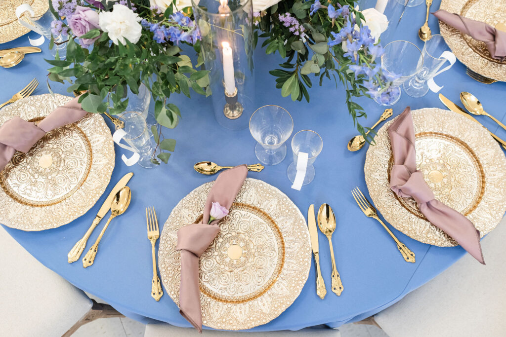 vintage wedding decor tablesetting with gold plates, blue lines and greenery