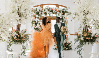African American bride and groom walk into stunning reception space. Bride wearing peach gown similar to Pantone's 2024 color of the year Peach Fuzz