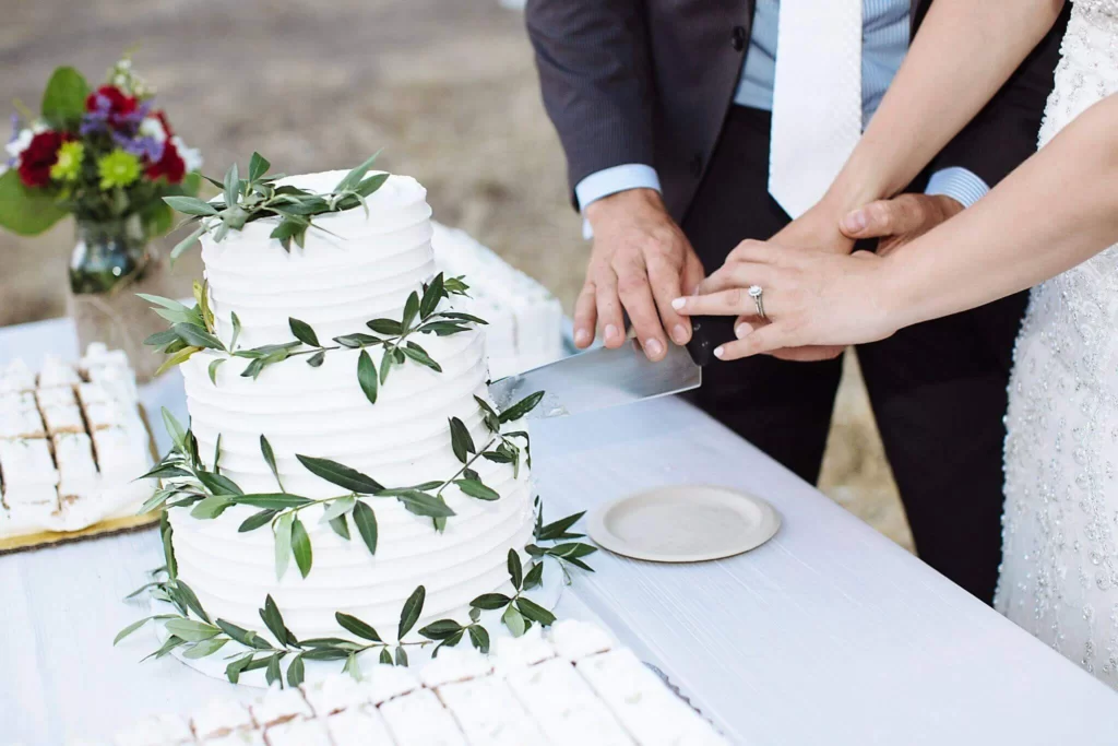 bride and groom cutting 3 tier white wedding cake with greenery accents