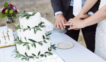 bride and groom cutting 3 tier white wedding cake with greenery accents wedding cake vendor Inclusive wedding cake options