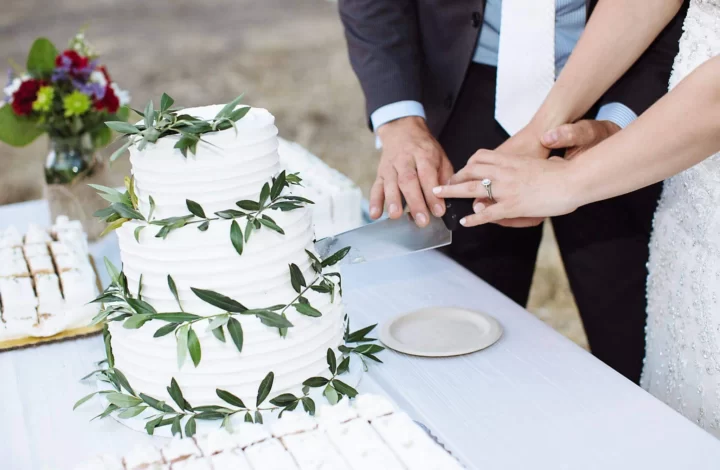 bride and groom cutting 3 tier white wedding cake with greenery accents wedding cake vendor Inclusive wedding cake options