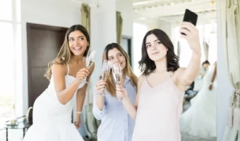 bridesmaid taking a selfie of bride and girls toasting champagne while trying on wedding dresses