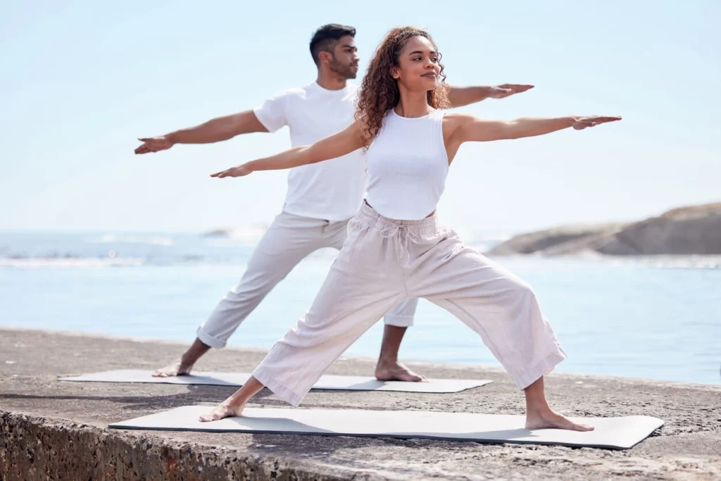 couple doing yoga next to water at couples wellness retreat