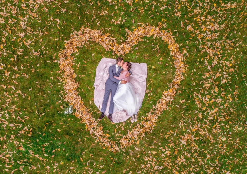 bride and groom laying on grass surrounded by a heart shape made from flowers for aerial drone wedding photography