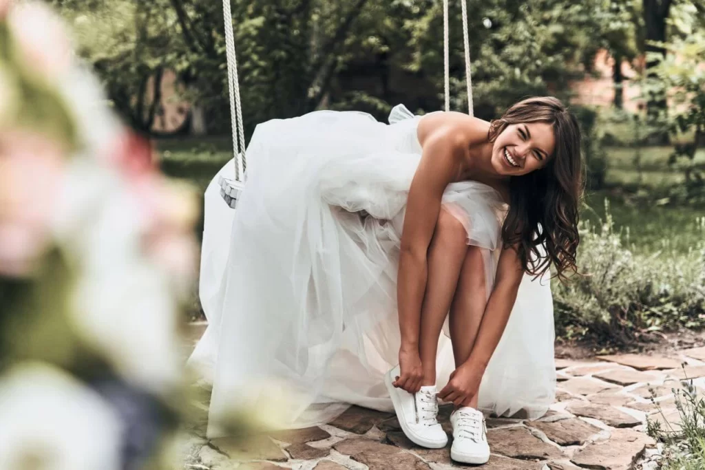 bride laughing while being photographed putting on her tennis shoes with her wedding dress