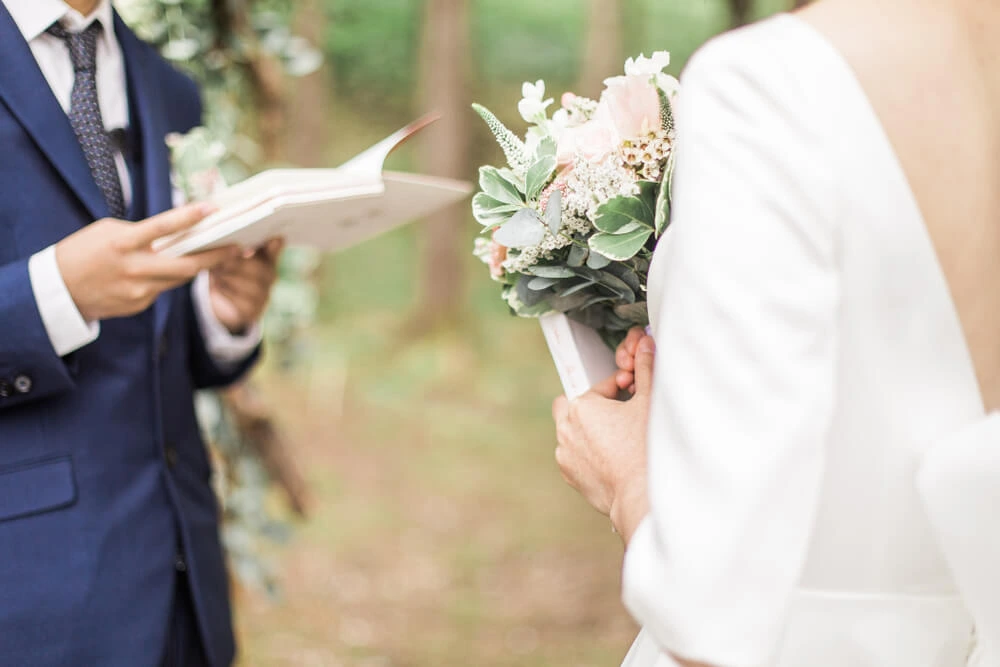 portrait of groom holding wedding vow card while bride listens