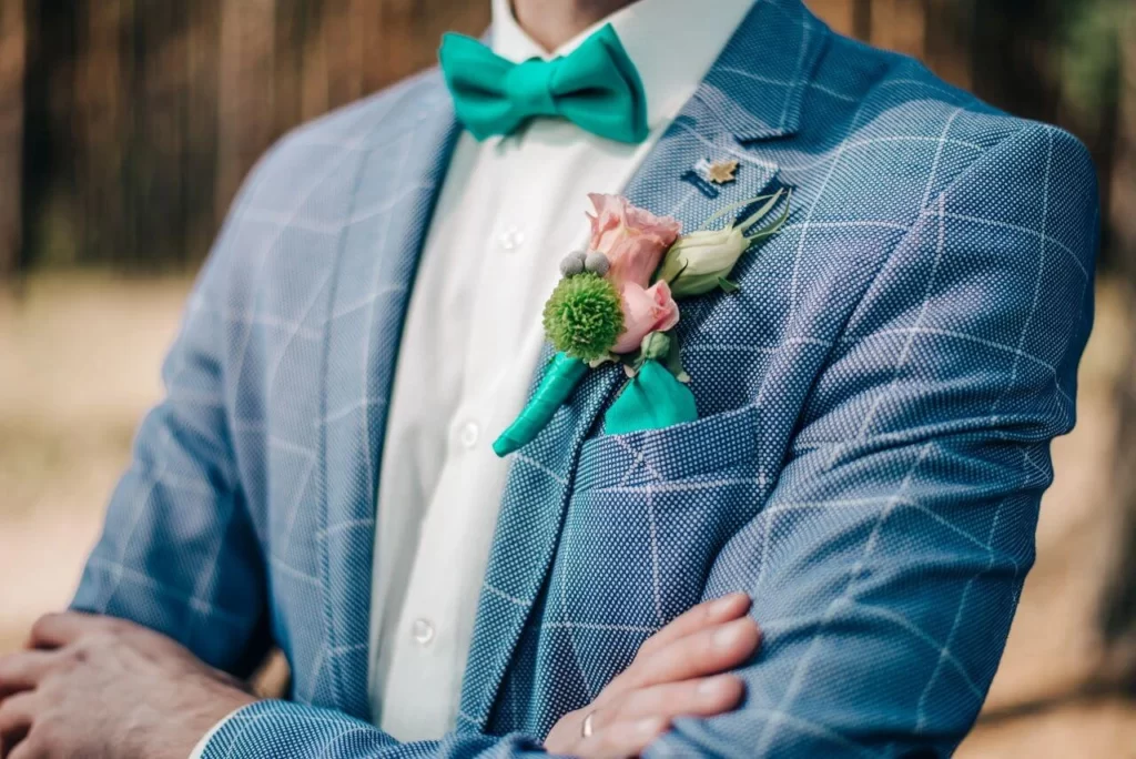 Groom in blue suit with checkered pattern posing outside with turquoise bow tie