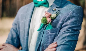 Groom in blue suit with checkered pattern posing outside with turquoise bow tie