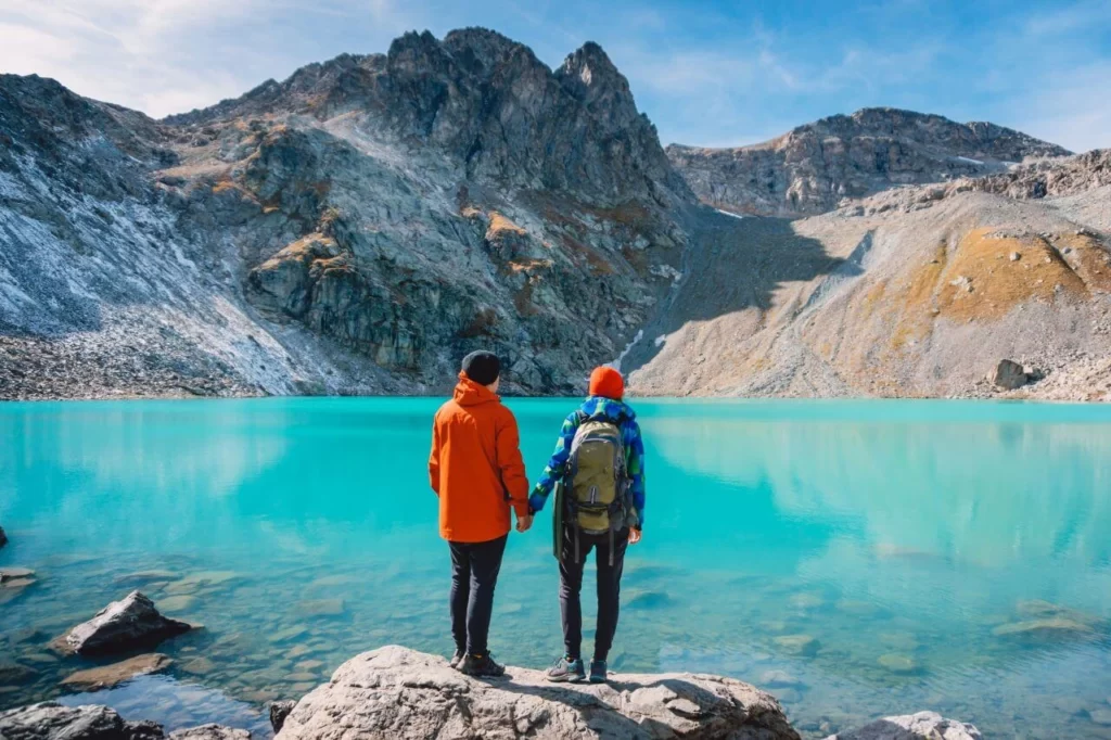 couple standing next to alpine lake admiring the beauty and mountains