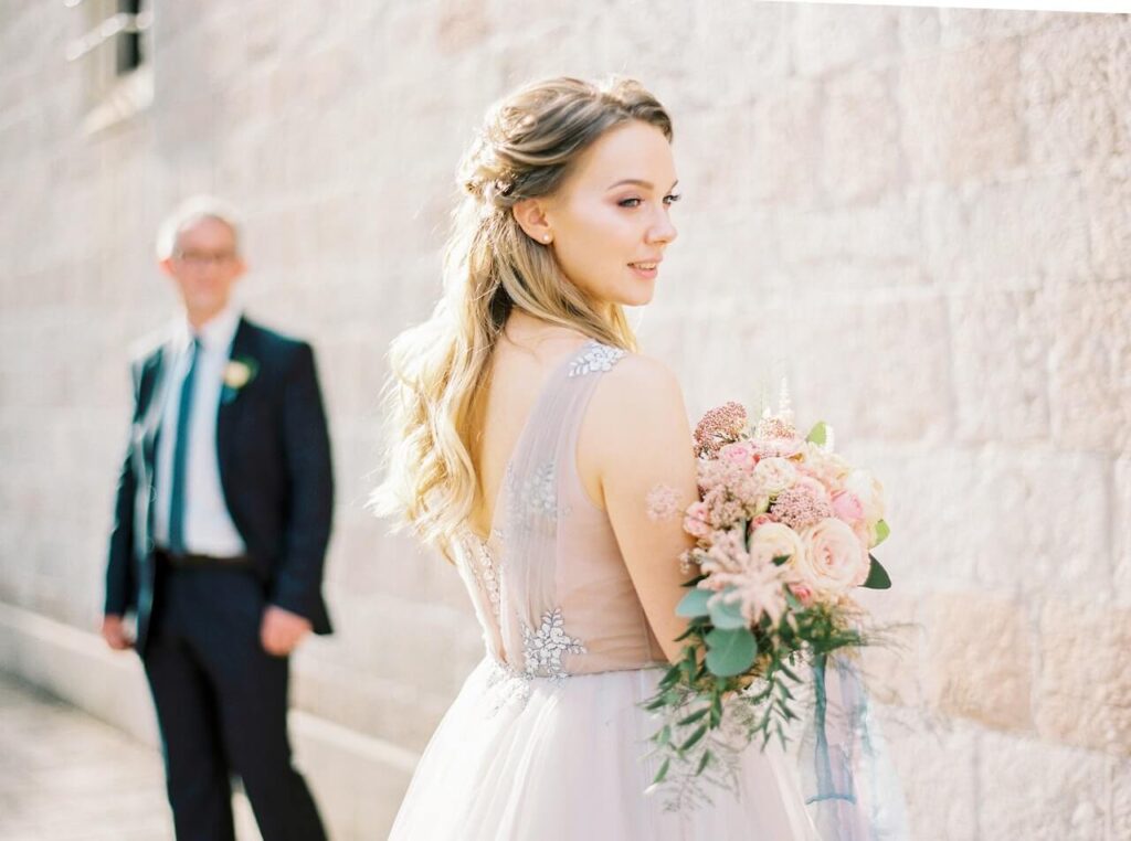 Beautiful bride holding bouquet for bridal portrait with groom standing in background