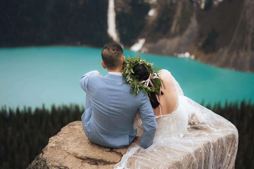 A bride and groom elope in the mountains of Canada overlooking Lake Louise in a wedding dress and blue suit