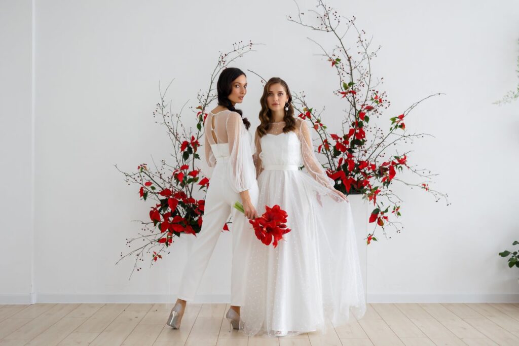two brides pose in front of amaryllis and poinsettia flower arrangement