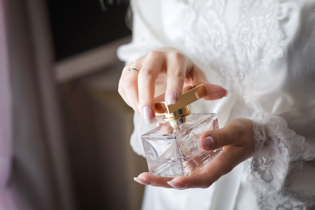 bride holding wedding perfume while wearing white robe with lace