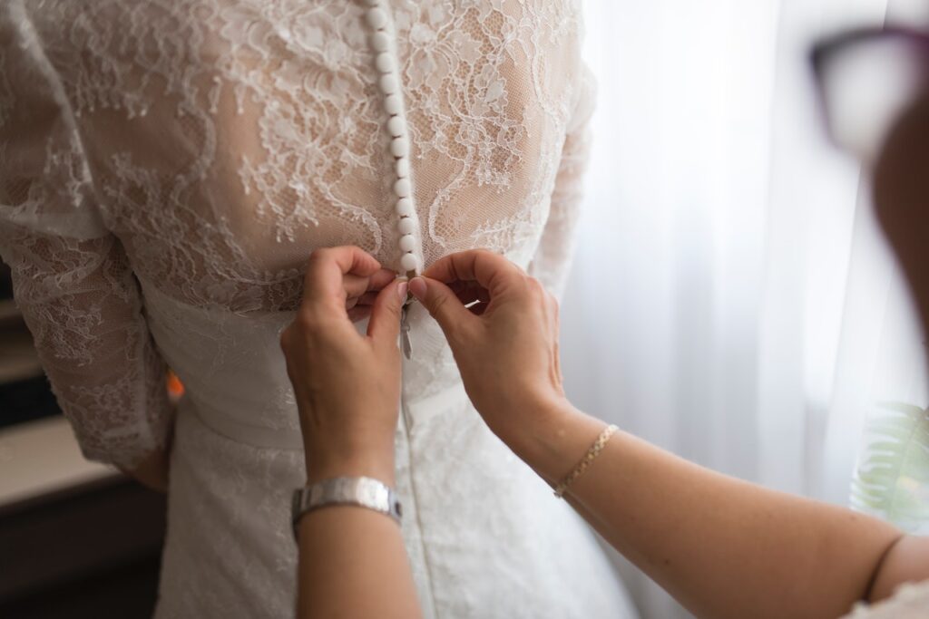 woman buttoning fabric covered buttons on wedding dress with chantilly lace embellishments