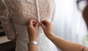 woman buttoning fabric covered buttons on wedding dress with chantilly lace embellishments