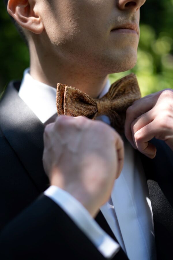 A groom, elegantly dressed in a suit and bow tie, meticulously adjusts his bow tie.