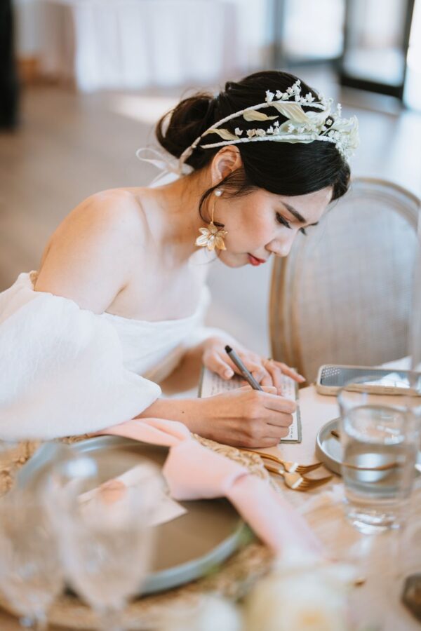 A bride, elegantly adorned in a white dress, gracefully writes on her wedding table.