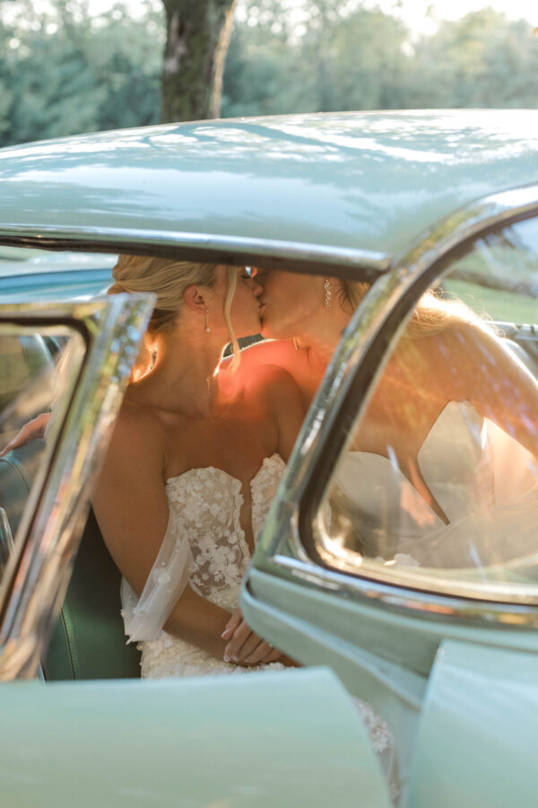 A newlywed couple shares a tender kiss inside a classic automobile