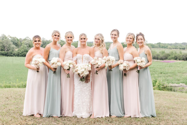A group of bridesmaids, elegantly dressed in pastel-colored gowns, stand together, striking a pose for a photograph.