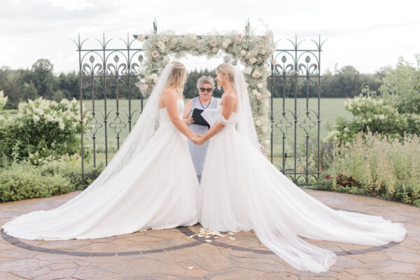 Two brides elegantly pose side by side, framed by a majestic archway.