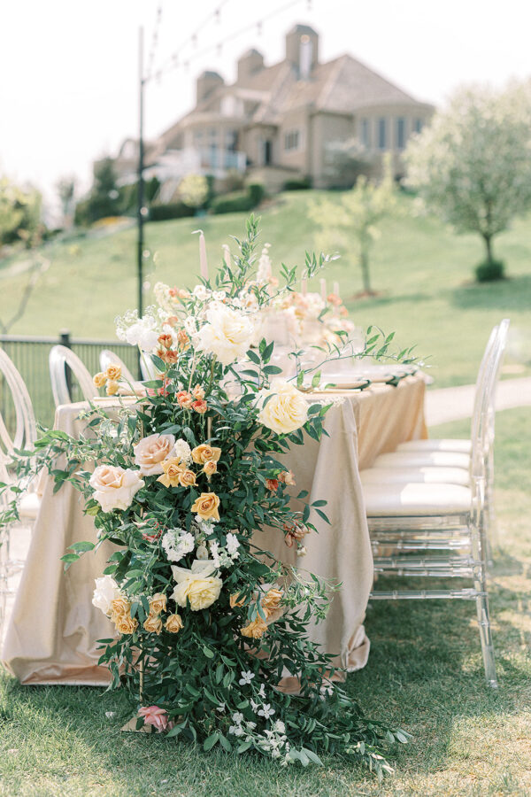 A tastefully arranged outdoor seating arrangement displaying a table adorned with beautiful flowers, flanked by chairs, set against the backdrop of a charming house.