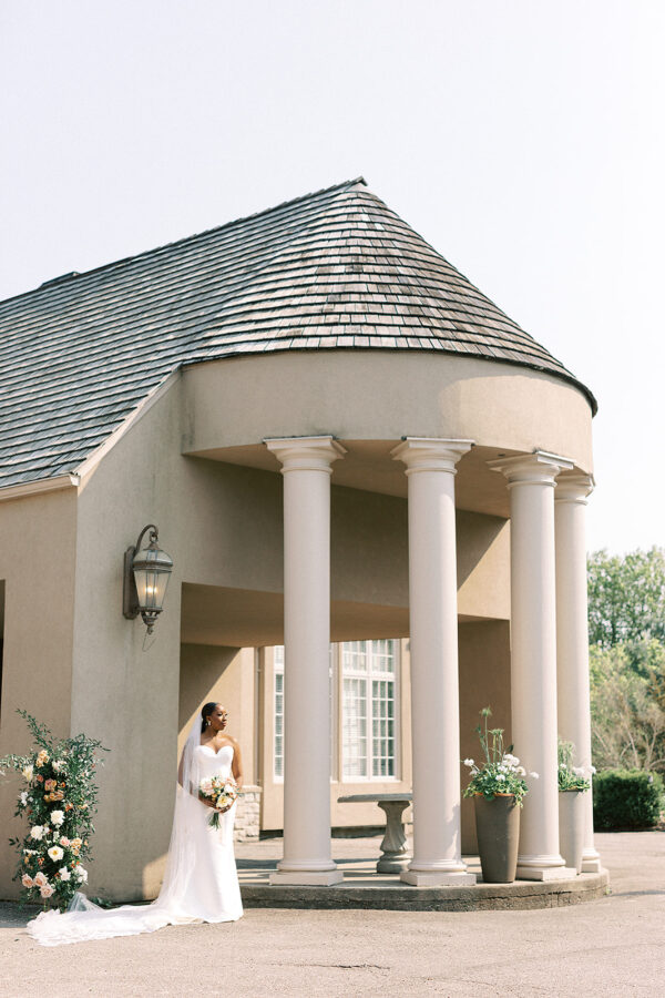In front of an impressive edifice, a bride stands gracefully, capturing a timeless moment.