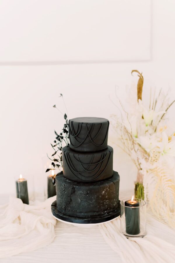 A black wedding cake elegantly displayed on a pristine white table, exuding sophistication and contrasting colors.