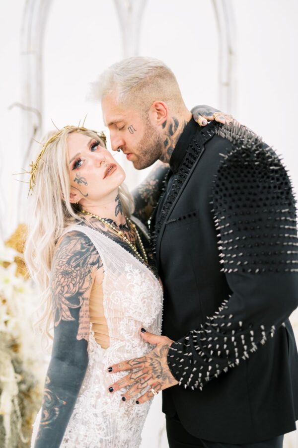 An elegant man in a suit accompanied by a woman adorned with intricate tattoos, embodying a blend of sophistication and edginess.