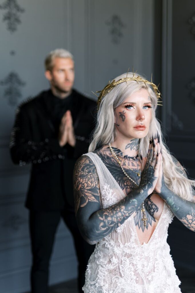An elegant man in a suit accompanied by a woman adorned with intricate tattoos, embodying a blend of sophistication and edginess.