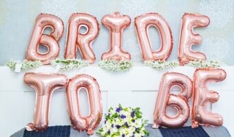 The image depicts a bed adorned with balloons that spell out 'bride to be'.