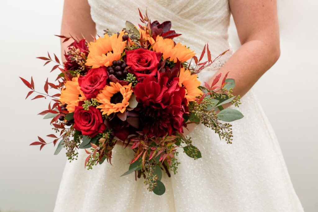 A bride gracefully holds a stunning bouquet of vibrant red and orange flowers