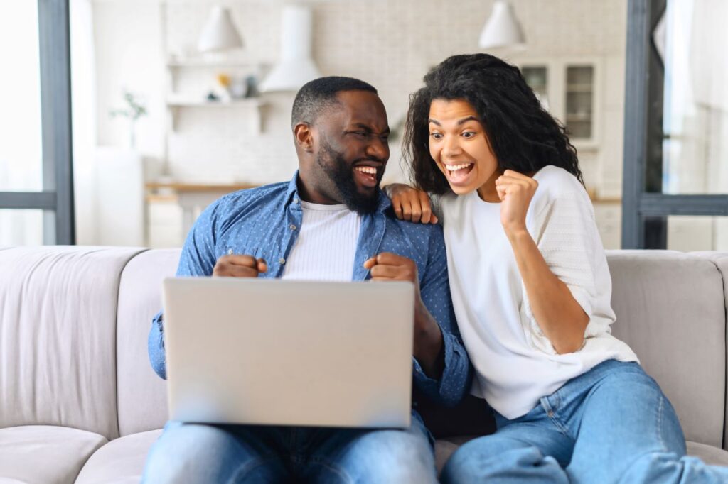 couple sitting on couch celebrating while checking their wedding registry gift purchases