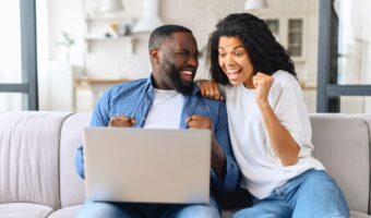 couple sitting on couch celebrating while checking their wedding registry gift purchases
