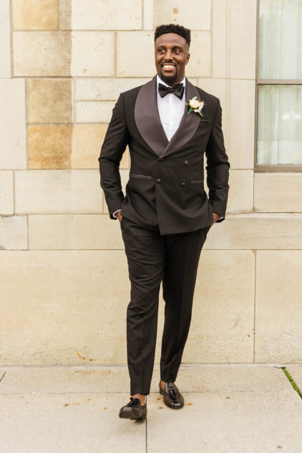 A well-dressed groom poses elegantly in a tuxedo for a photograph, exuding style and confidence.