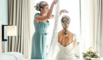 bride sitting on bed while mother of the bride puts veil on her