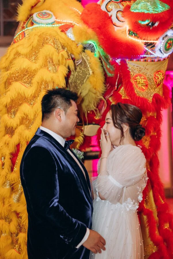 bride laughs while posing with groom in front of lion dancers