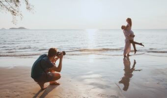 newlyweds pose on beach while photographer capture beautiful image during honeymoon photo shoots