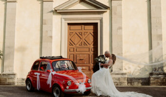 Chelsea and Michael's iconic picture outside Italy intimate wedding chapel with vintage car and veil blowing in wind