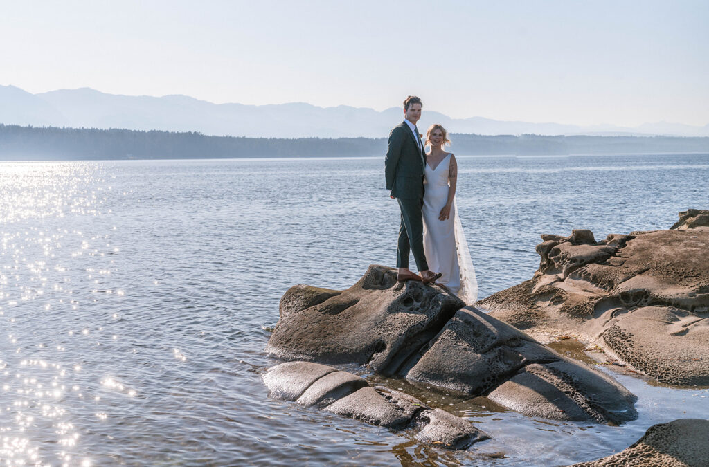 bride and groom posing on the rocks next to the water at wedding on Hornby Island