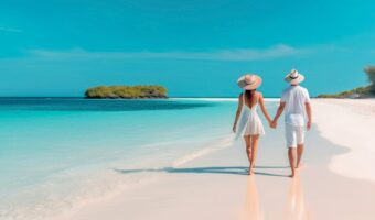 couple walking on beach holding hands next to turquoise water at destination wedding trends
